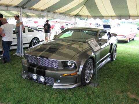 1991 Ford LTD Crown Victoria - gray late-model Ford Mustang with black racing stripes, billet grille and body kit displayed on grass under a tent at a car show.