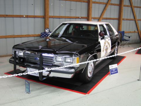 1991 Ford LTD Crown Victoria - black and white Ford Highway Patrol sedan fitted with a front push bar and pillar spotlight, parked on a red display mat.