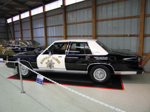 1991 Ford LTD Crown Victoria - Side profile of a black and white Highway Patrol sedan with gold star shield and Safety and Service lettering along the rear door.