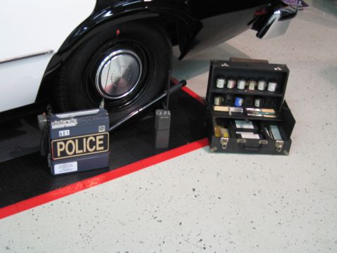 1991 Ford LTD Crown Victoria - black radar or radio unit marked POLICE and an open metal tool box sit on the floor beside a black-and-white cruiser's tire.