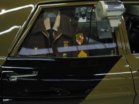 1991 Ford LTD Crown Victoria - brown trooper uniform with a Maryland shoulder patch and sergeant chevrons is displayed inside the rear window of a patrol car.