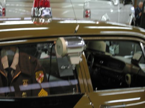 1991 Ford LTD Crown Victoria - Through a tan patrol car window, a brown uniform with a Maryland patch is visible alongside a chrome side-mounted spotlight.