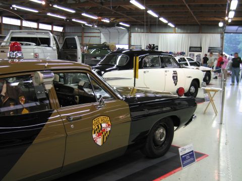 1991 Ford LTD Crown Victoria - tan and black Maryland State Police car with shoulder-patch door shield sits in the foreground of a hall of vintage police cars.