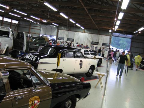 1991 Ford LTD Crown Victoria - black and white POLICE sedan and a tan trooper car are displayed among other vehicles as visitors walk through the exhibit hall.
