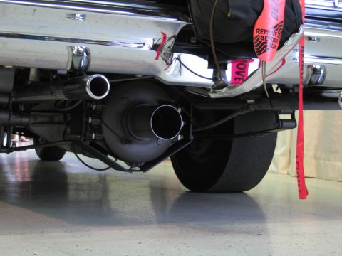 1991 Ford LTD Crown Victoria - Low-angle underside view of a car's chrome bumper, polished dual exhaust tips and a red drag parachute pack.