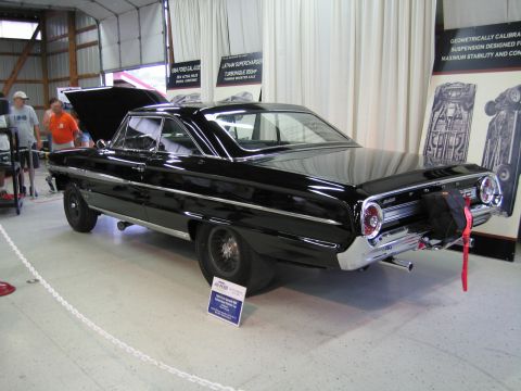 1991 Ford LTD Crown Victoria - Rear quarter view of a black Ford full-size two-door hardtop with its hood up and a parachute pack, displayed in an exhibit hall.