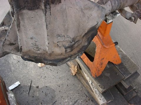 1987 Ford Bronco - Close-up of a differential housing supported by an orange jack stand and wooden blocks.