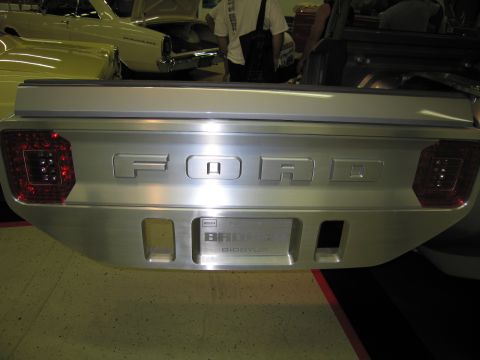 1991 Ford LTD Crown Victoria - Polished aluminum tailgate panel embossed with FORD lettering, flanked by round LED taillights, on a custom vehicle indoors.