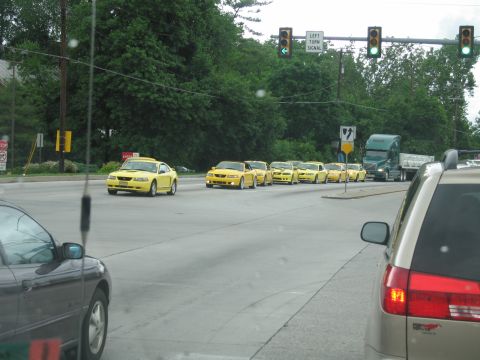 1991 Ford LTD Crown Victoria - Convoy of bright yellow sports cars stopped at a traffic-light intersection, viewed through a vehicle windshield with a semi nearby.