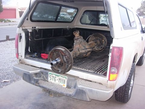 1987 Ford Bronco - A white pickup truck carries a differential and brake assemblies in its bed, with a license plate visible.