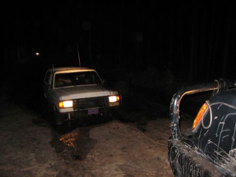 1989 Ford Bronco - A white SUV, likely from the late 1980s, is being towed at night through a muddy area.