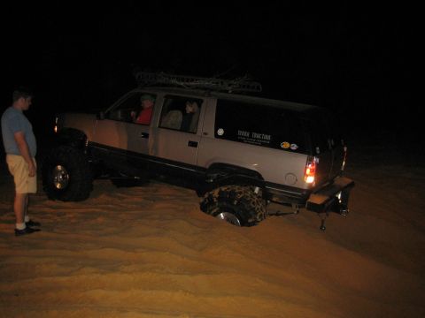 1989 Ford Bronco - A lifted SUV is stuck in the sand at night, with people inside and one person standing nearby.