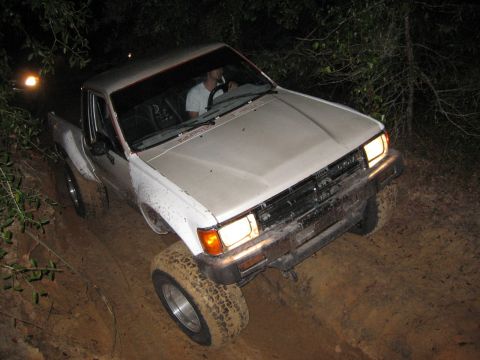1989 Ford Bronco - White pickup truck navigates a challenging muddy trail in the dark, its off-road capabilities.