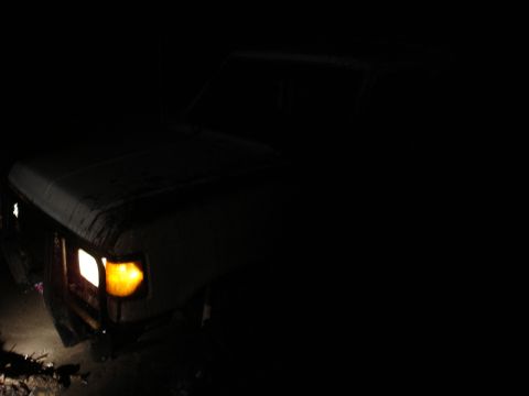 1989 Ford Bronco - A 1989 Ford Bronco is seen from the front-three-quarter angle at night, its headlights illuminating the dark surroundings.
