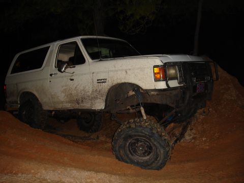 1989 Ford Bronco - A white 1989 Ford Bronco navigates a muddy, off-road terrain at night.