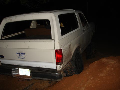 1989 Ford Bronco - This white SUV is stuck in a muddy ditch at night. A 'Blue Ridge 4x4' sticker is visible on the rear.