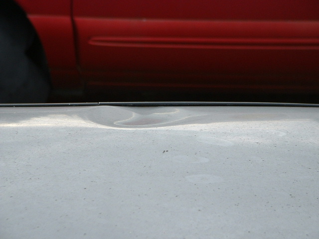 Close-up of a dent in a gray body panel next to a red vehicle