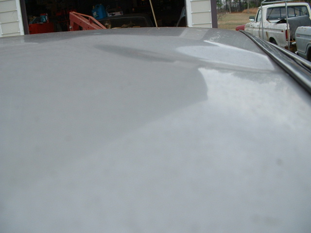 Close-up of gray painted roof or panel with vehicles in background