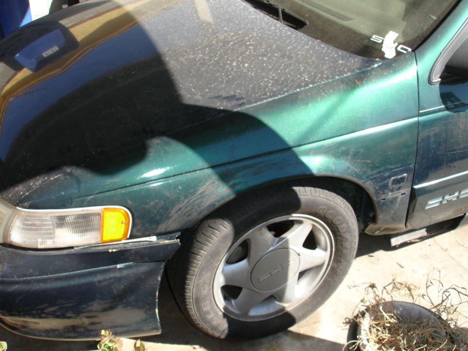 Dark green SHO sedan front corner, dusty paint, headlight and silver five-spoke wheel