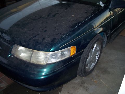 1995 Ford Taurus - Front passenger side of a dusty 1995 Ford Taurus, showing the headlight and fender.