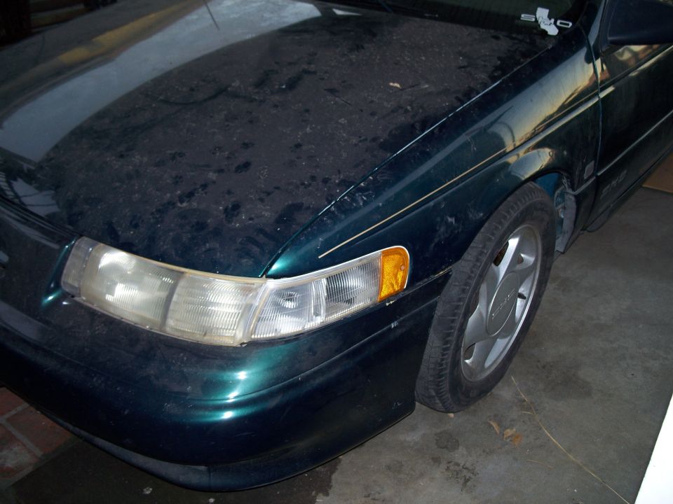 Dark green 1995 Ford Taurus front fender and headlight assembly, covered in dust