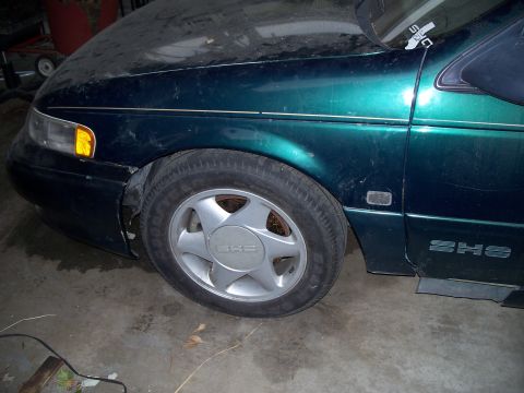 1995 Ford Taurus - The front fender and wheel of a green car are visible, SHO badging on the lower door panel.