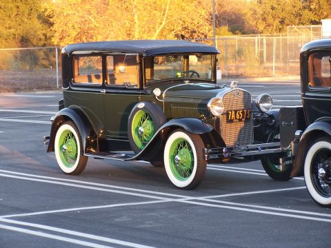1990 Ford Bronco - A vintage green sedan, possibly from the 1930s, is parked in a lot next to another car, its bright green wheels and whitewall tires visible.