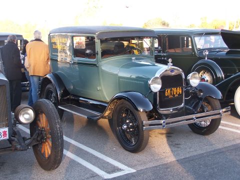 1990 Ford Bronco - A 1929 Ford Model AA truck, likely a panel delivery van, is parked in a lot with other classic vehicles.