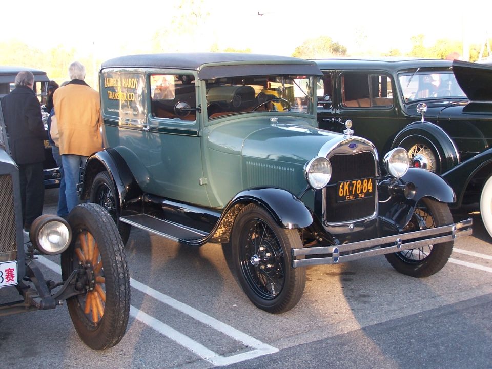 1929 Ford Model AA truck with Laurel & Hardy Transfer Co. lettering on door, parked next to other vintage cars