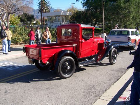1990 Ford Bronco - A classic red Ford pickup truck is seen from the rear-three-quarter view, driving on a sunny day.