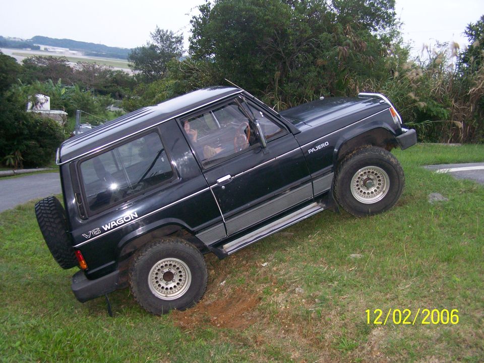 Black 2-door Mitsubishi Pajero V6 Wagon SUV on a grassy slope, side view, spare tire on rear