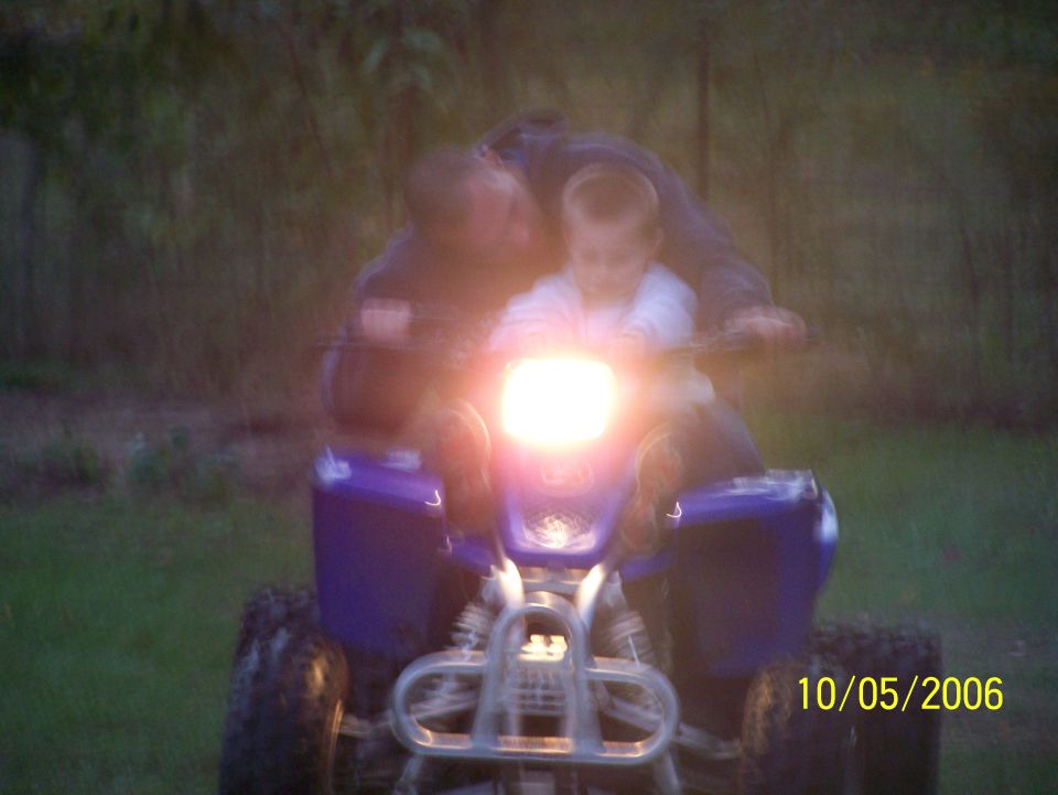 Blue Yamaha ATV at dusk, headlight on, adult and child riding, front view