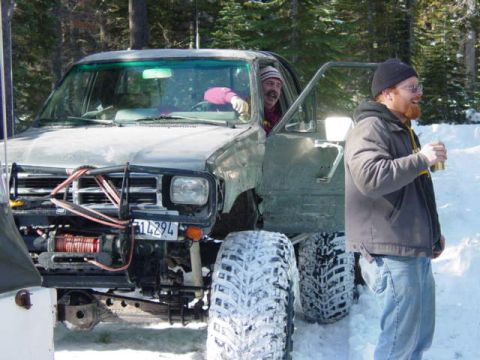 1986 Ford Bronco - Two men stand next to a modified truck in a snowy, wooded area.