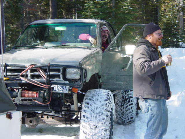 guy with beard holding drink next to lifted truck with winch in snow