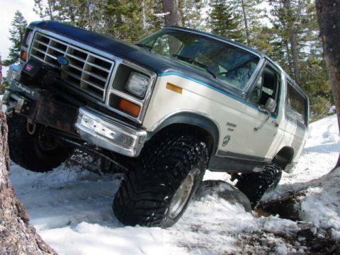 1986 Ford Bronco - A two-tone white and blue Ford Bronco navigates a snowy, wooded terrain.