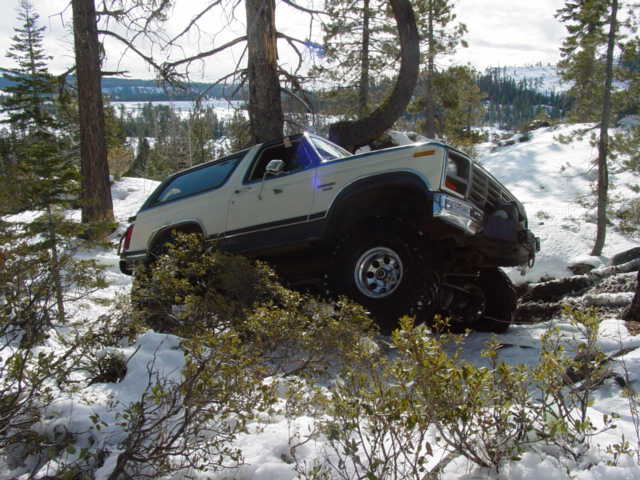 White Ford Bronco with lifted suspension driving off-road in a snowy forest