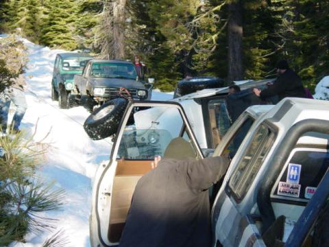 1986 Ford Bronco - Several off-road vehicles are stuck in a snowy, wooded area, with people attempting to free them.