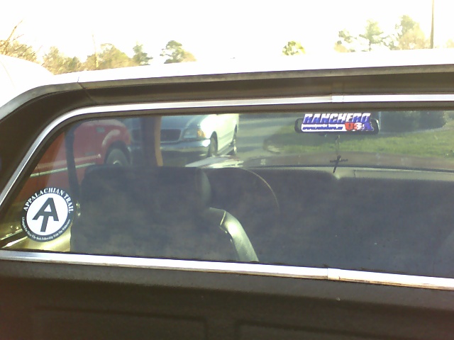 Interior view of a vehicle showing the rear window with 'Ranchero' and 'Appalachian Trail' stickers. Other vehicles are visible through the window