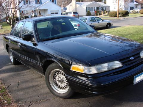 2003 Ford Crown Victoria - A black Ford Crown Victoria is parked in front of houses on a street.