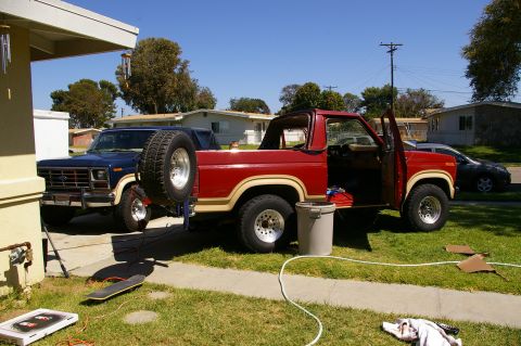 1986 Ford Bronco - A red 1986 Ford Bronco is parked in a driveway with its doors open, and a blue Ford pickup truck is behind it.