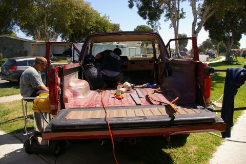 1986 Ford Bronco - Two people are working on the interior of a red pickup truck, with tools and cleaning supplies visible.
