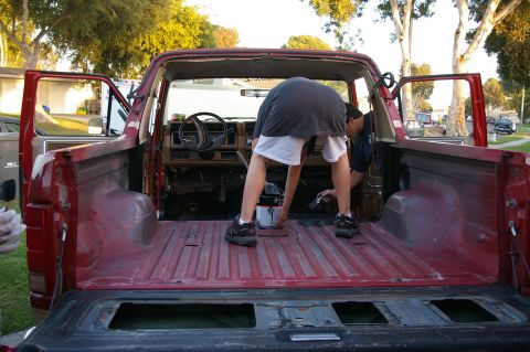1986 Ford Bronco - Someone is applying a coating to the bed of a red pickup truck.