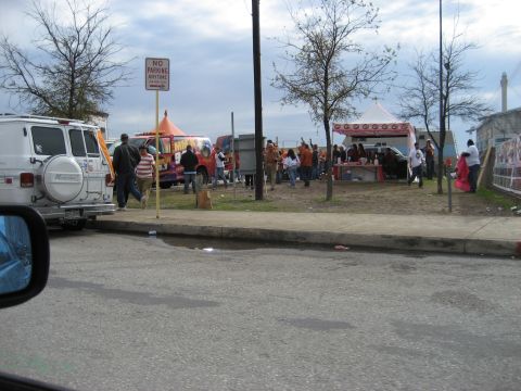 1986 Ford Bronco - A white van is parked on the side of the road near a gathering with food trucks and tents.
