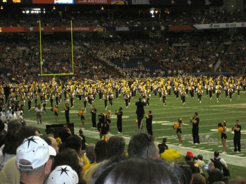 1986 Ford Bronco - A marching band performs on a football field during the Alamo Bowl, with spectators in the stands.