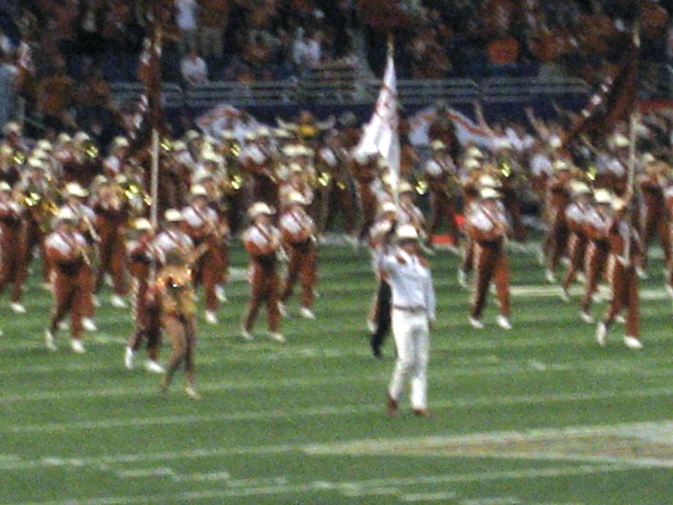 marching band in uniform on a football field with flags and instruments
