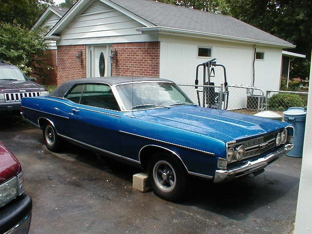 Blue vintage two-door hardtop coupe with black vinyl top parked in driveway by a garage