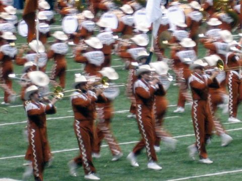1986 Ford Bronco - A marching band performs on a football field, with members playing brass instruments and wearing distinctive uniforms.