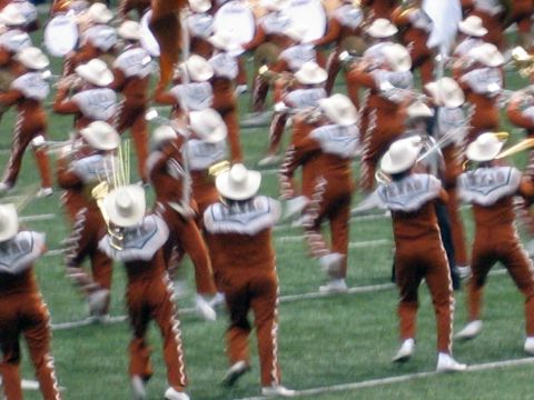 1986 Ford Bronco - A marching band in distinctive uniforms and cowboy hats performs on a grassy field, likely during a sporting event.