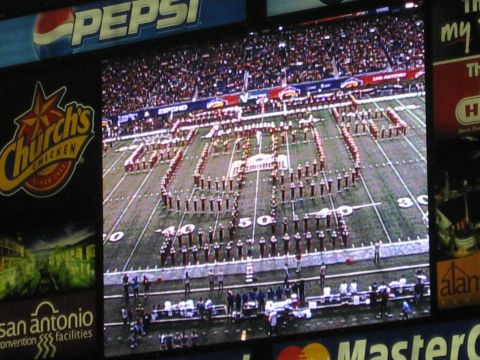 1986 Ford Bronco - A marching band forms the text '2006 ALAMO BOWL' on a football field, with stadium advertisements in the background.