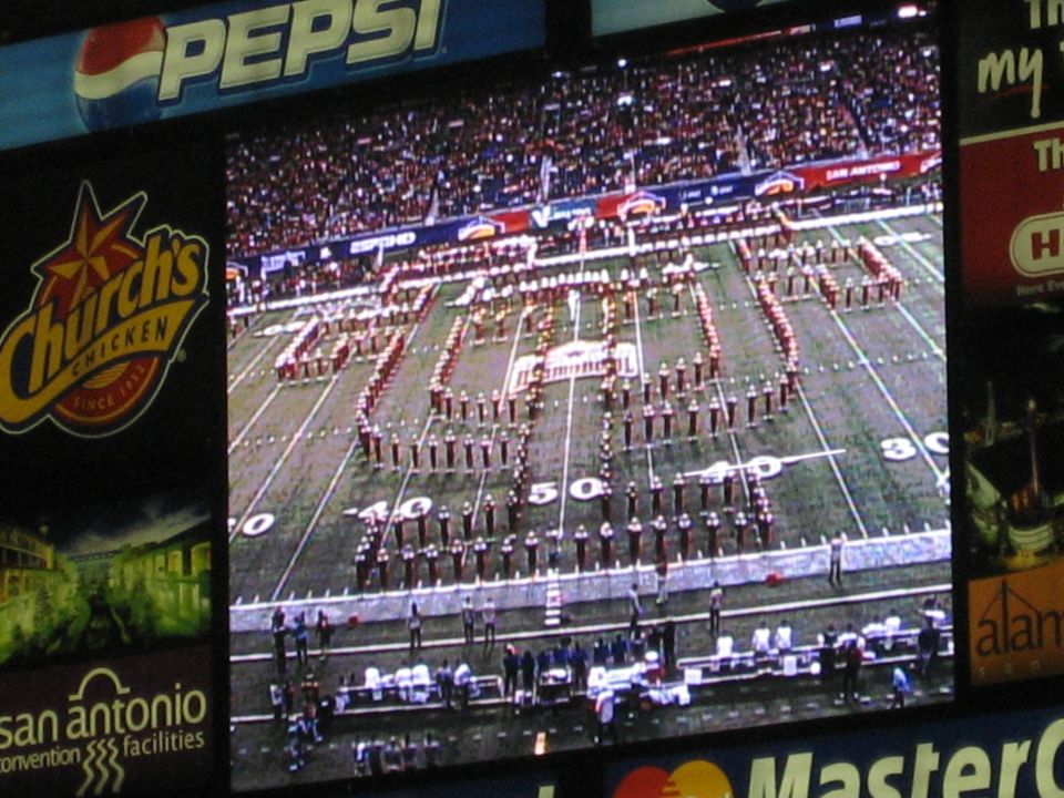Marching band on football field spelling out '2006 ALAMO BOWL' with Pepsi and Church's Chicken logos visible